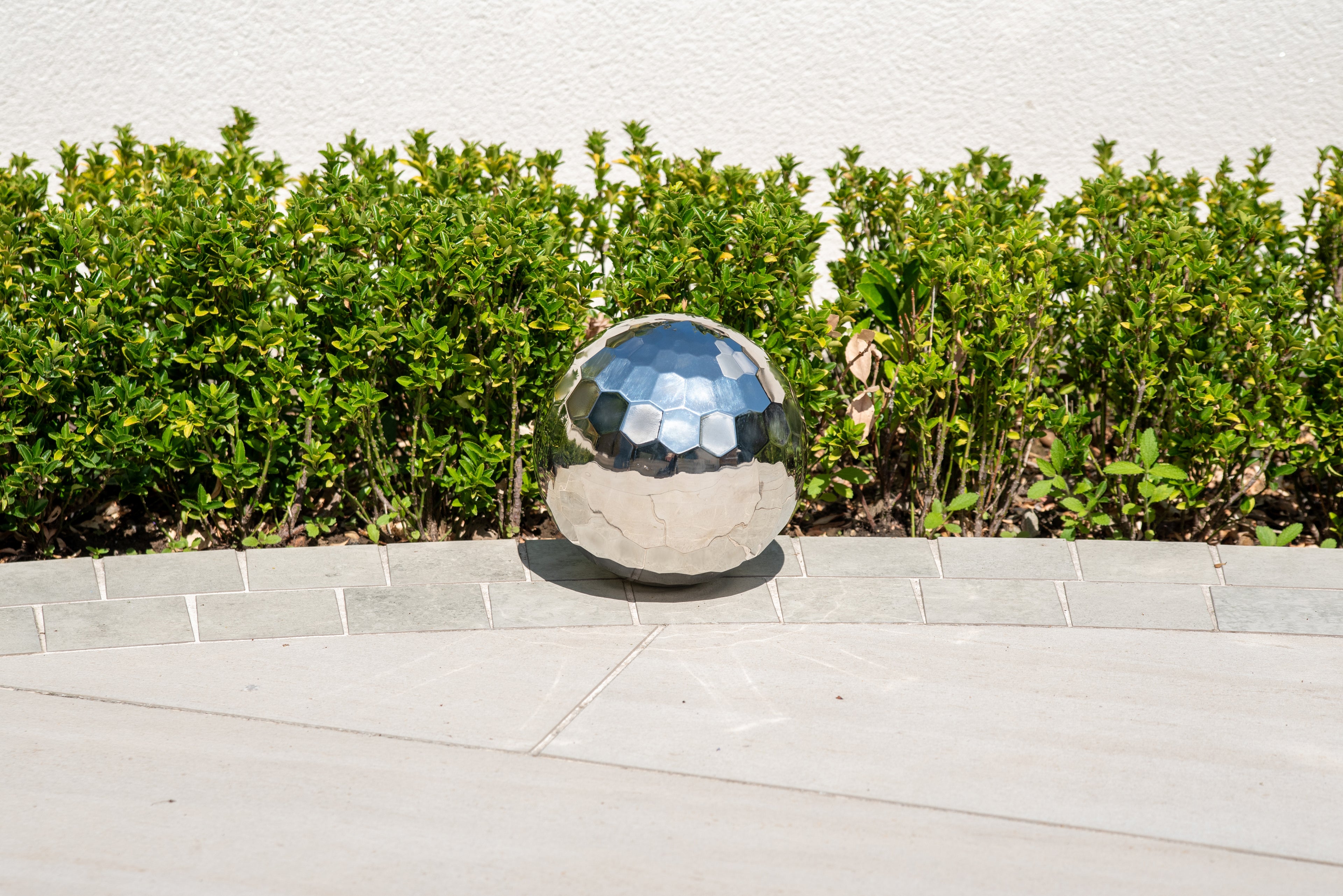 Reflective silver steel tumble ball on a concrete ledge, faceted mirrored surface