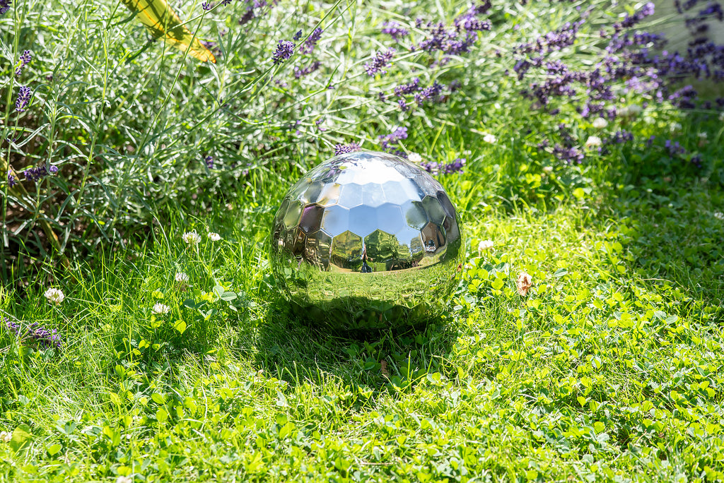 Reflective steel tumble ball on grass with faceted mirrored design