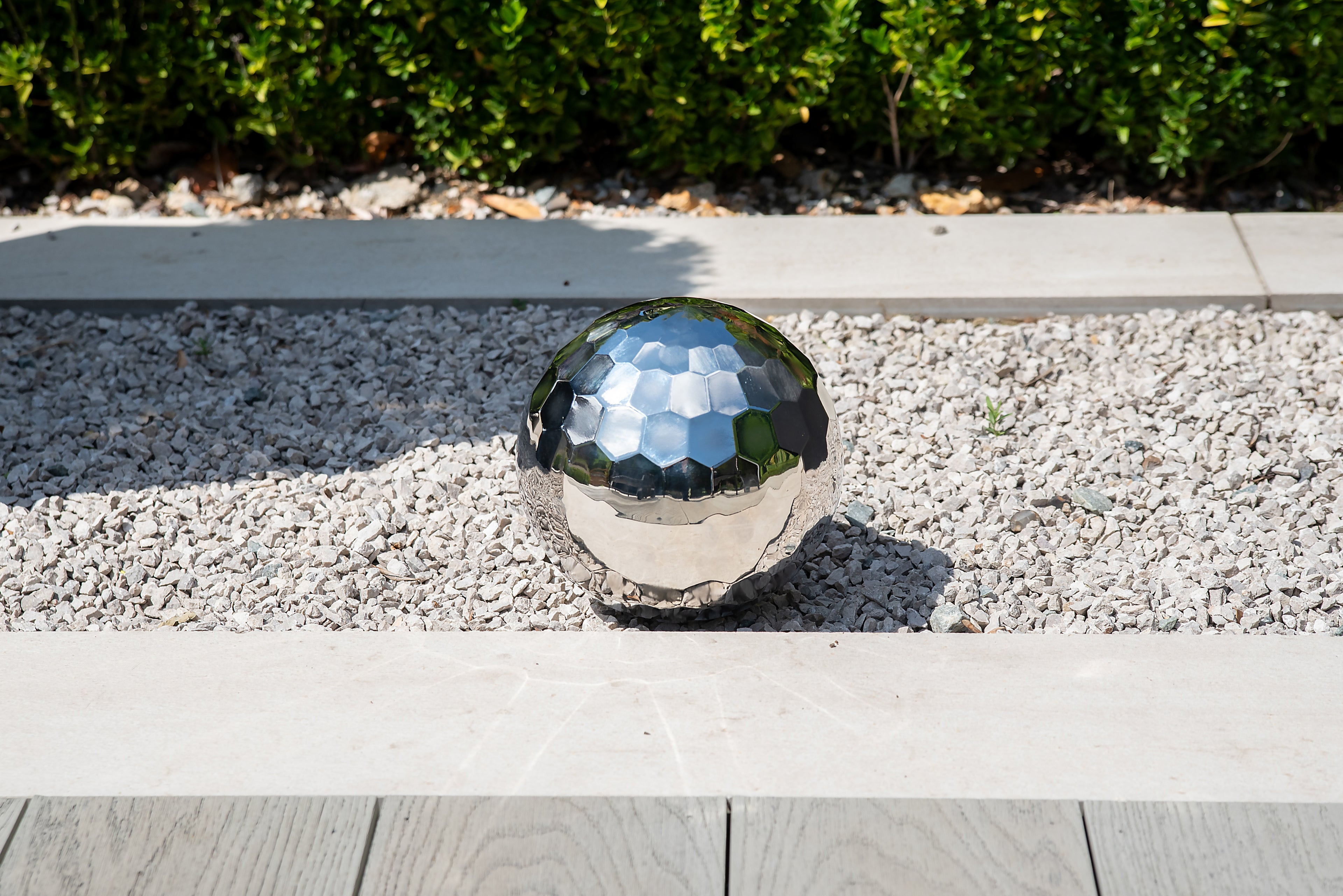 Reflective silver steel tumble ball with faceted surface on gravel edge