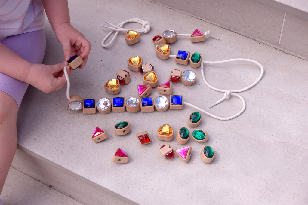 Person holding a lacing jewel; scattered blue squares, pink triangles, green ovals, gold hearts