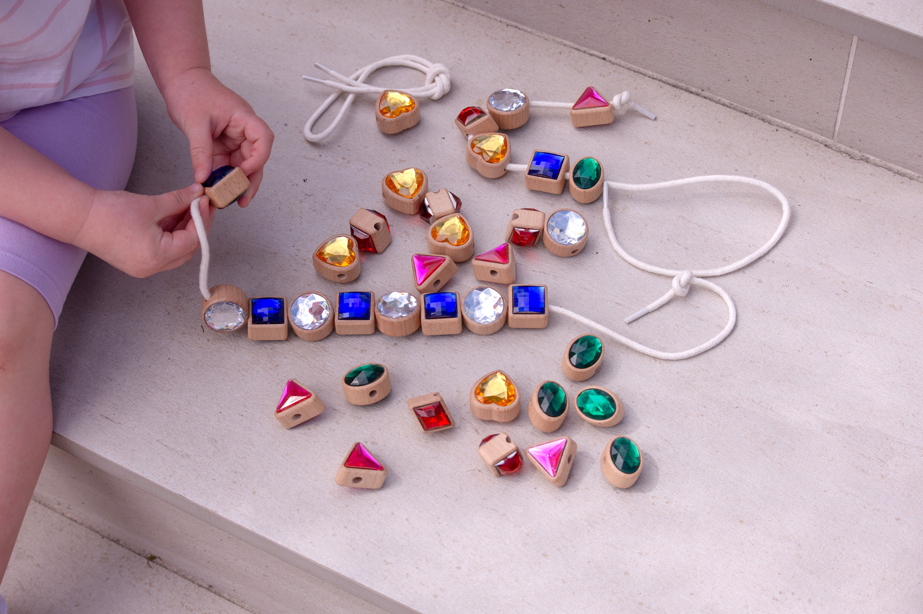Person holding a lacing jewel; scattered blue squares, pink triangles, green ovals, gold hearts