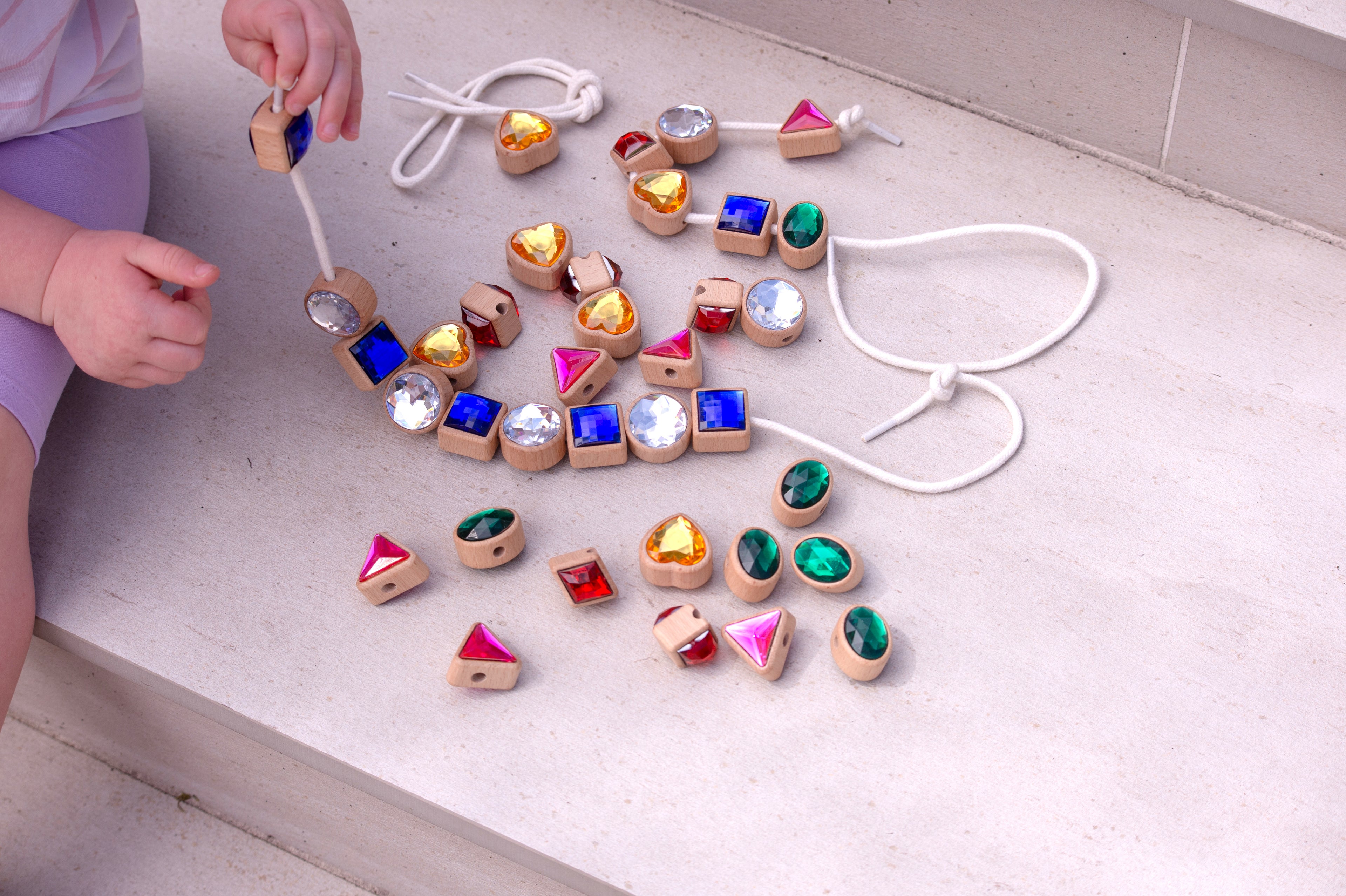 Shape lacing jewels on cords: blue squares, pink triangles, green ovals and gold heart beads