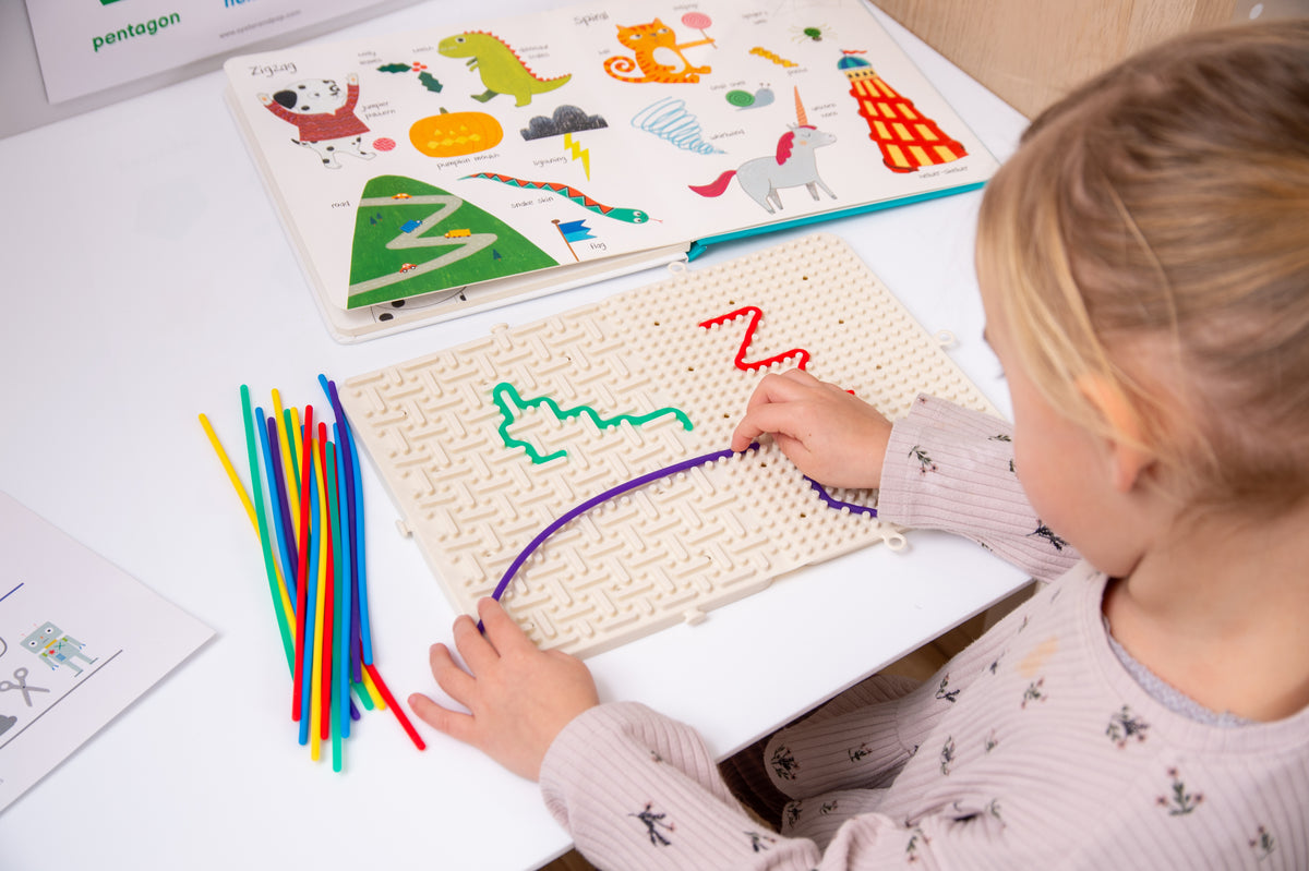 Beige activity maze board with colorful route outlines and rainbow sticks on tabletop