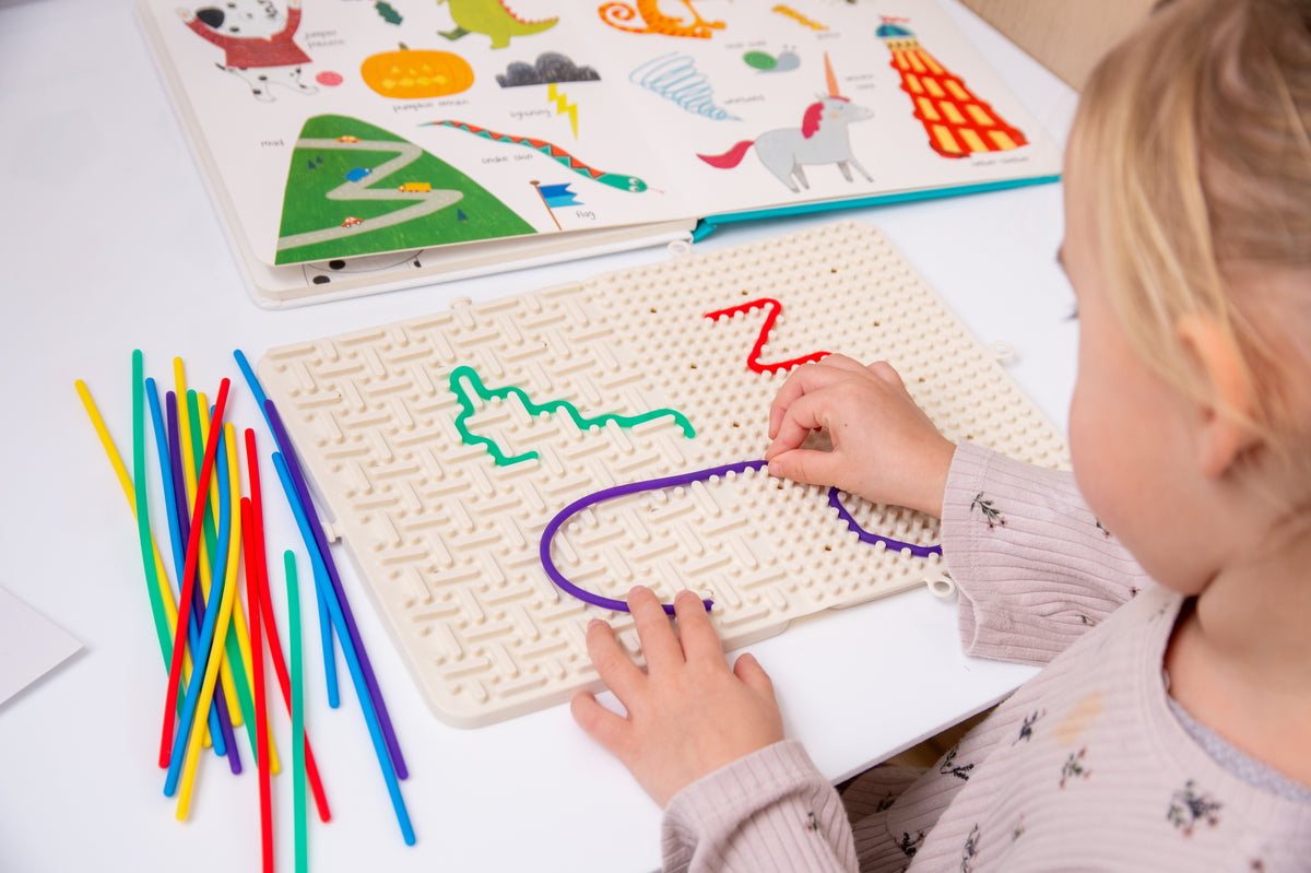 Beige activity maze board with colorful route lines and rainbow sticks, child hands