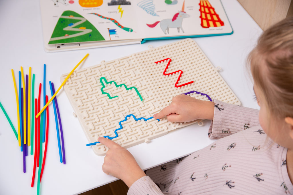 Beige activity maze board with colorful route outlines and rainbow sticks, hands playing