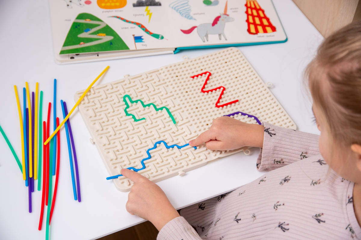 Beige activity maze board with colorful route outlines and rainbow sticks, hands playing