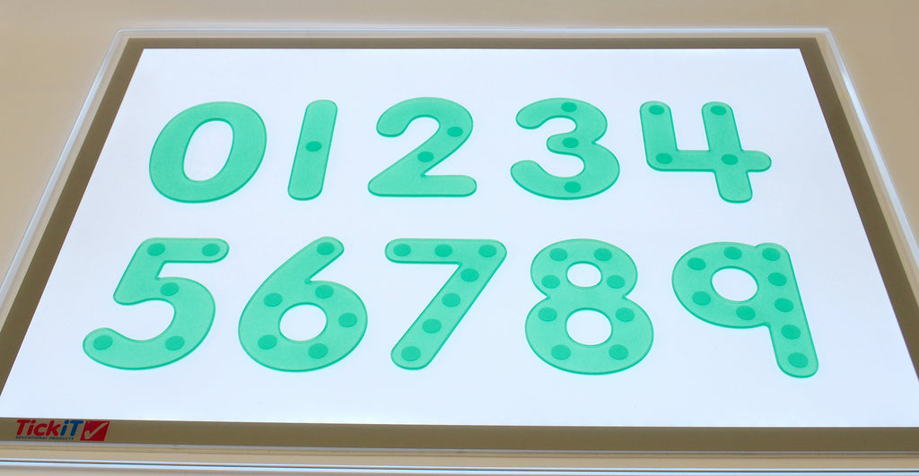 Close-up of green dot number tiles on a white board with digits 0 to 9