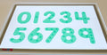 Close-up of green dot number tiles on a white board with digits 0 to 9
