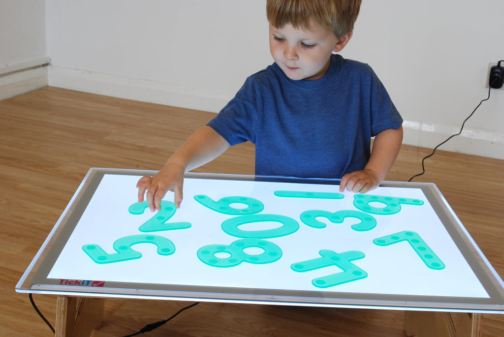 Child arranging green dot number tiles on a white learning board