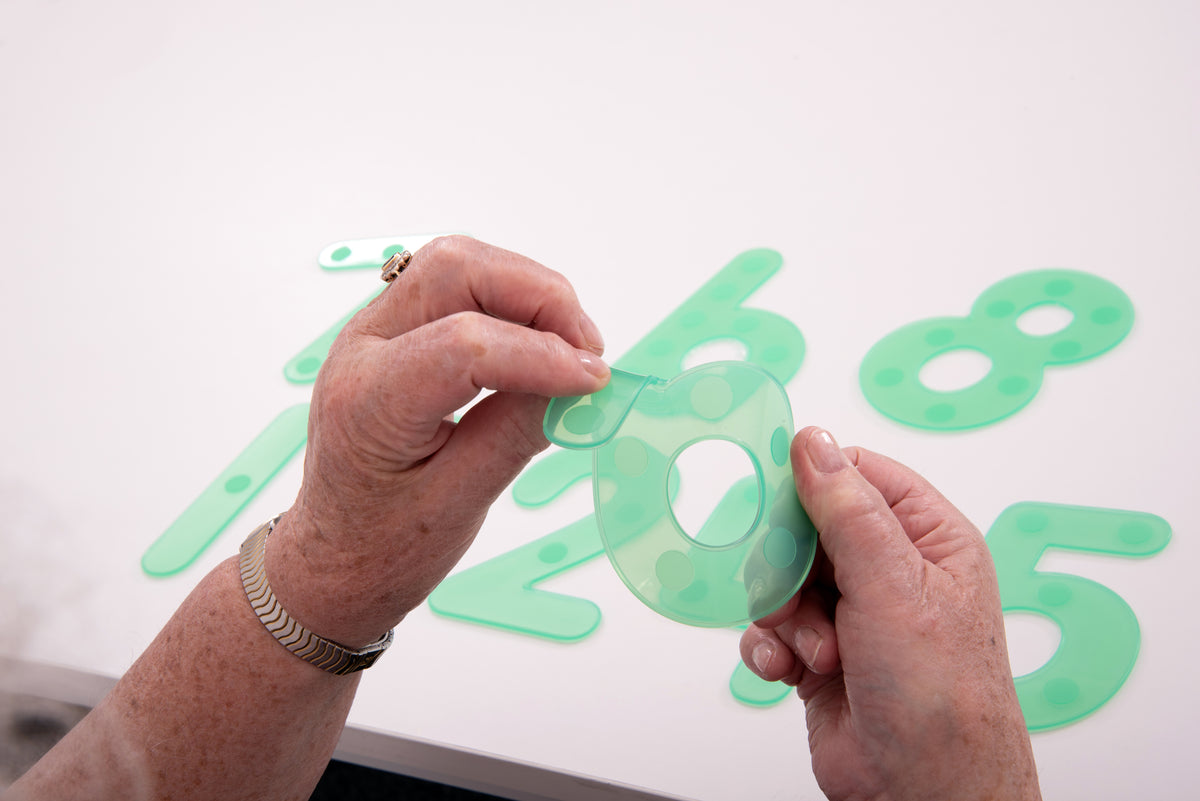 Hands positioning a green dot number tile on a white number layout