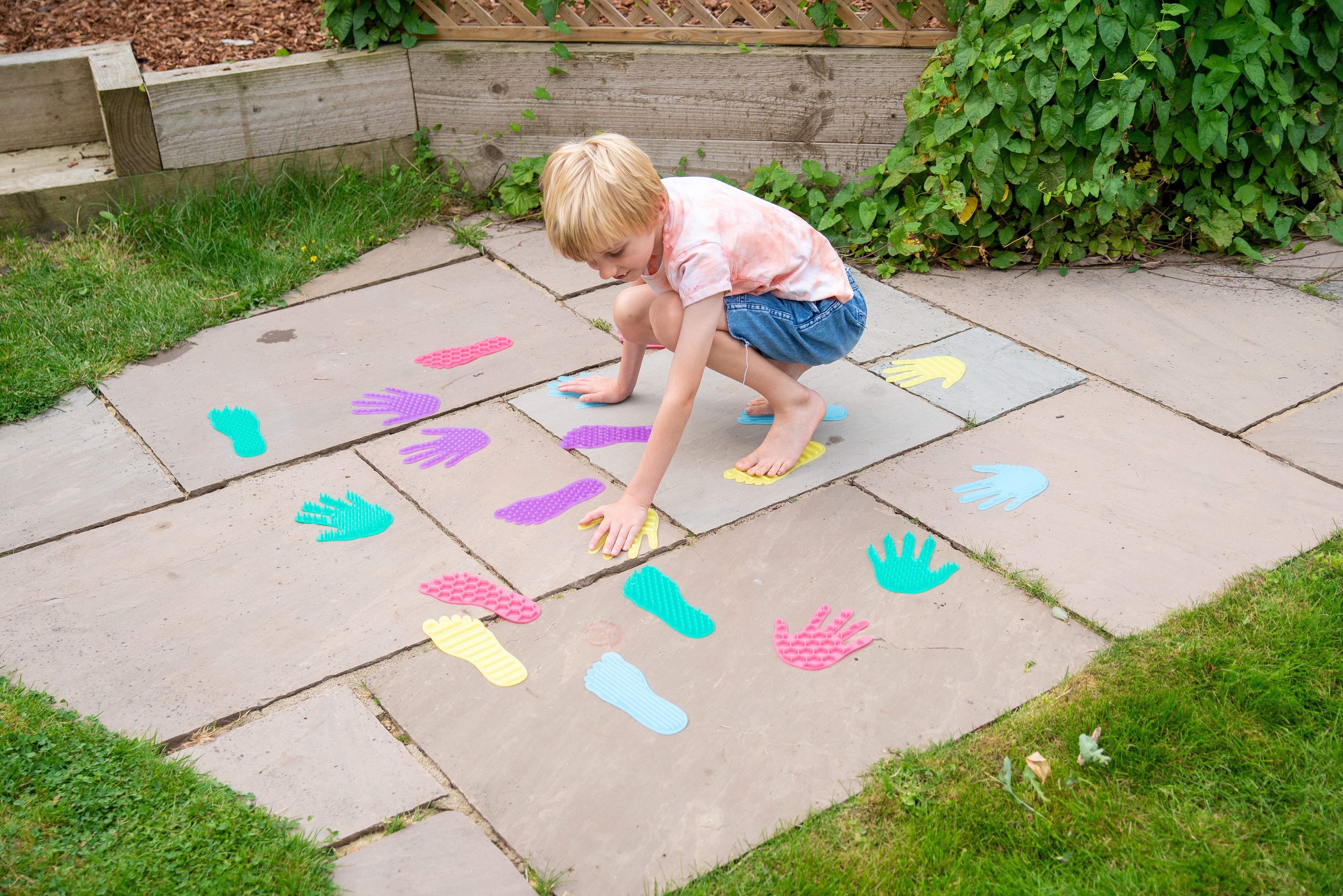 Child crawling on patio tiles with colorful hand and foot stickers spread out
