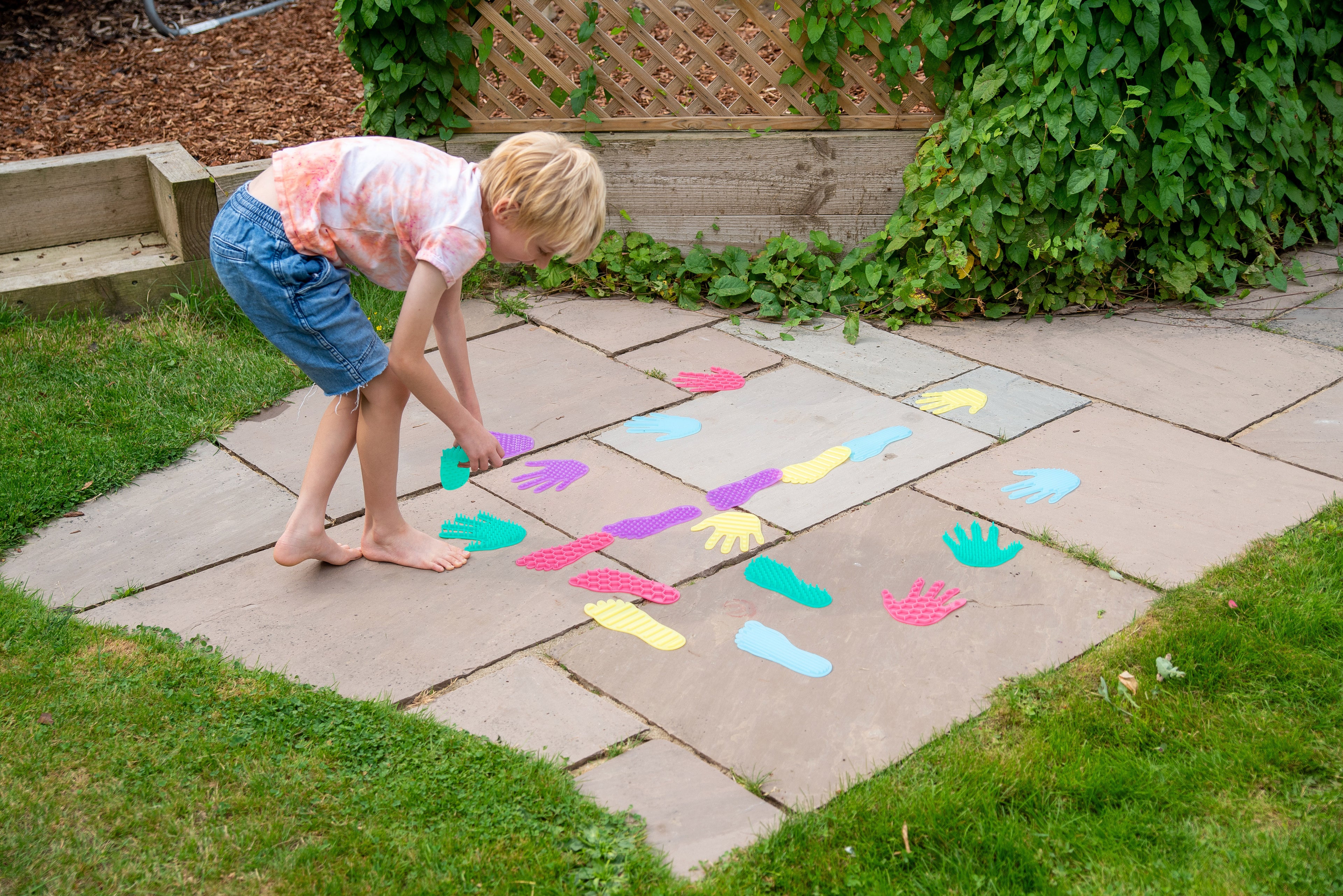 Young child kneeling on patio with colorful hand and foot stickers scattered on tiles