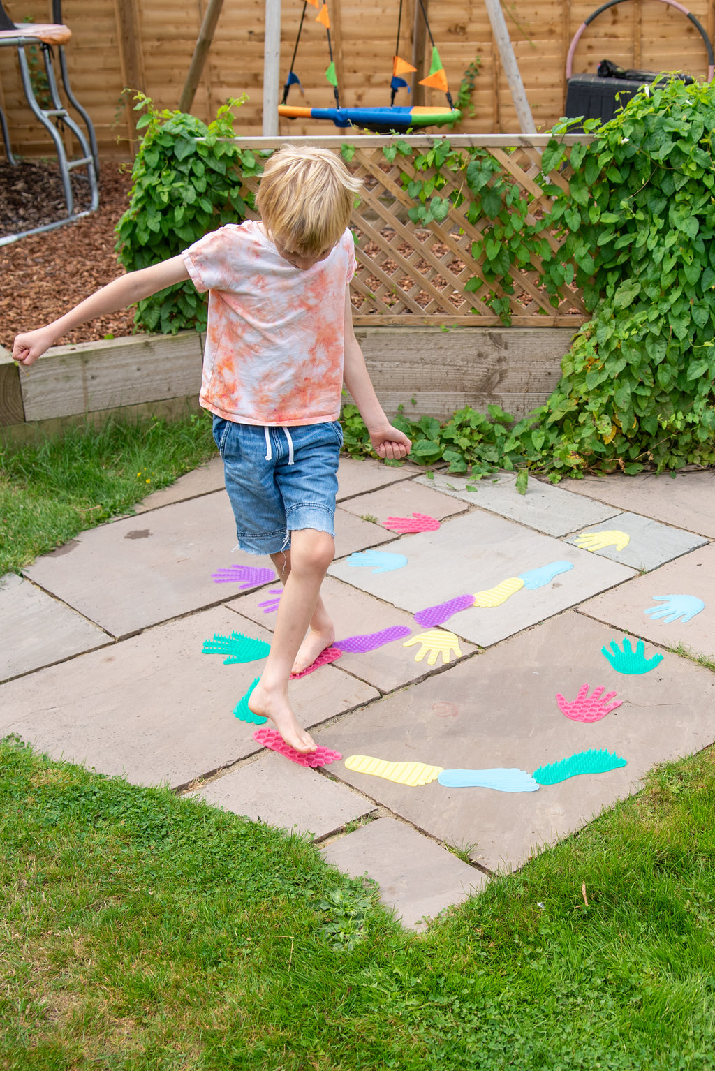Young child standing on outdoor patio tiles covered with colorful hand and foot stickers