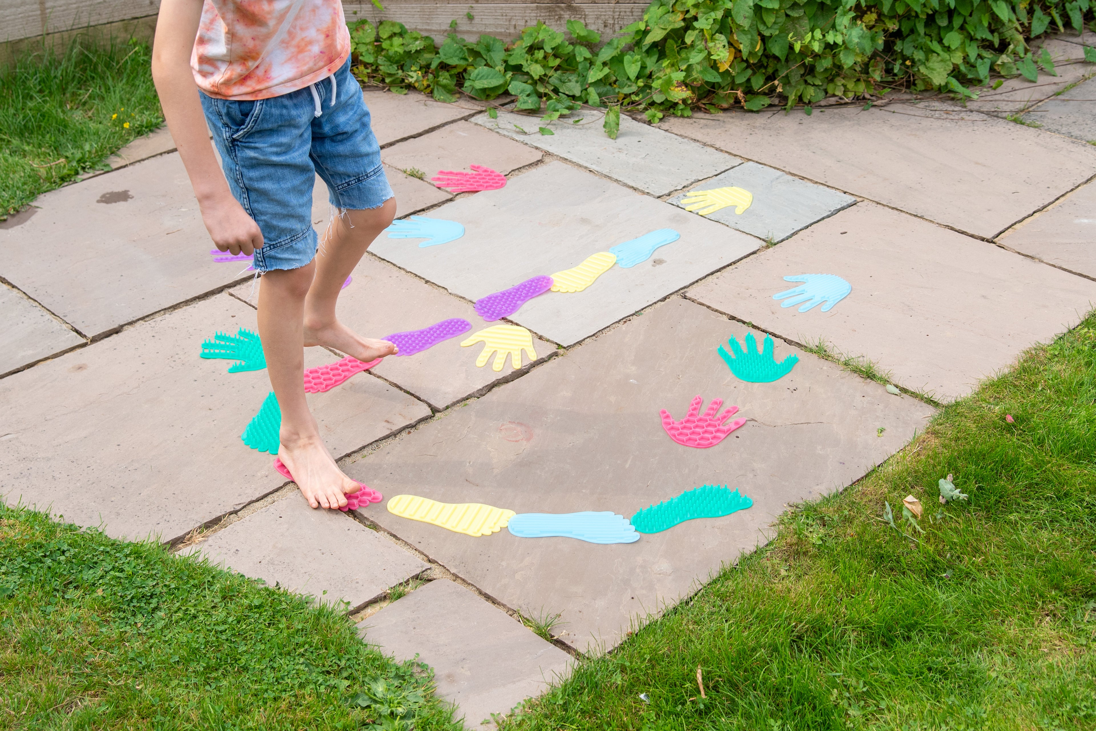 Child playing with colorful hand and foot stickers on outdoor patio tiles