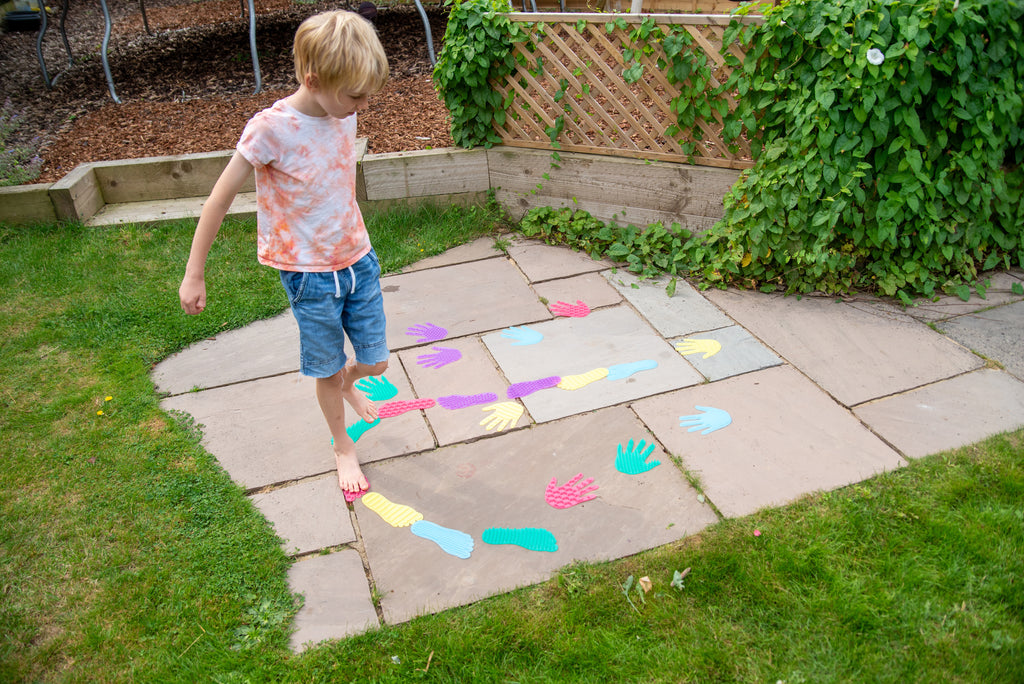 Child stepping across colorful hand and foot stickers on backyard patio tiles