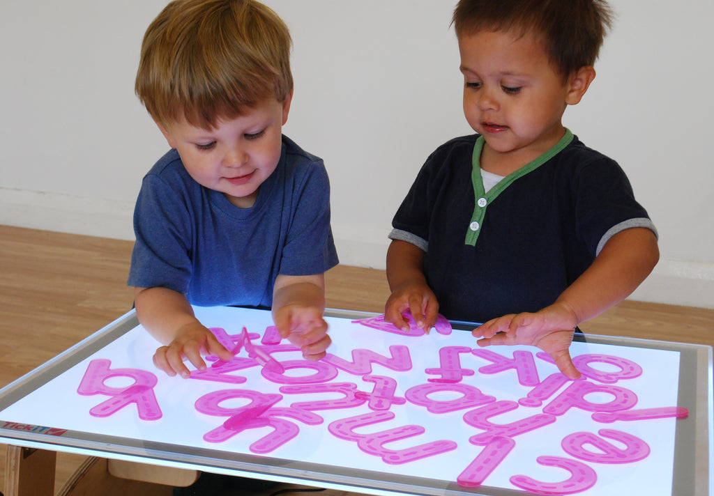 Alphabet tracing activity with two children placing pink letter shapes