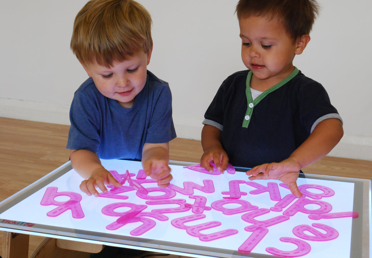 Alphabet tracing activity with two children placing pink letter shapes