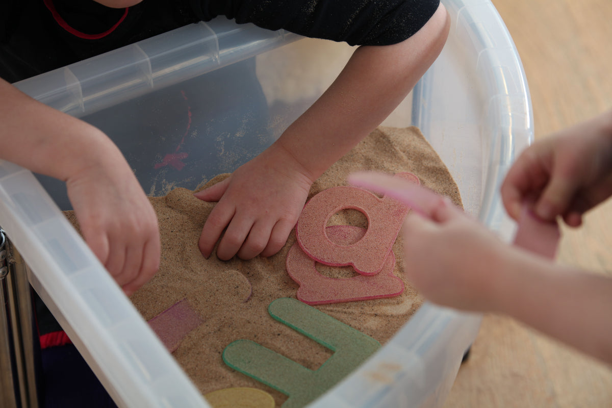 Alphabet tracing tray with foam letter cutouts and hands placing shapes