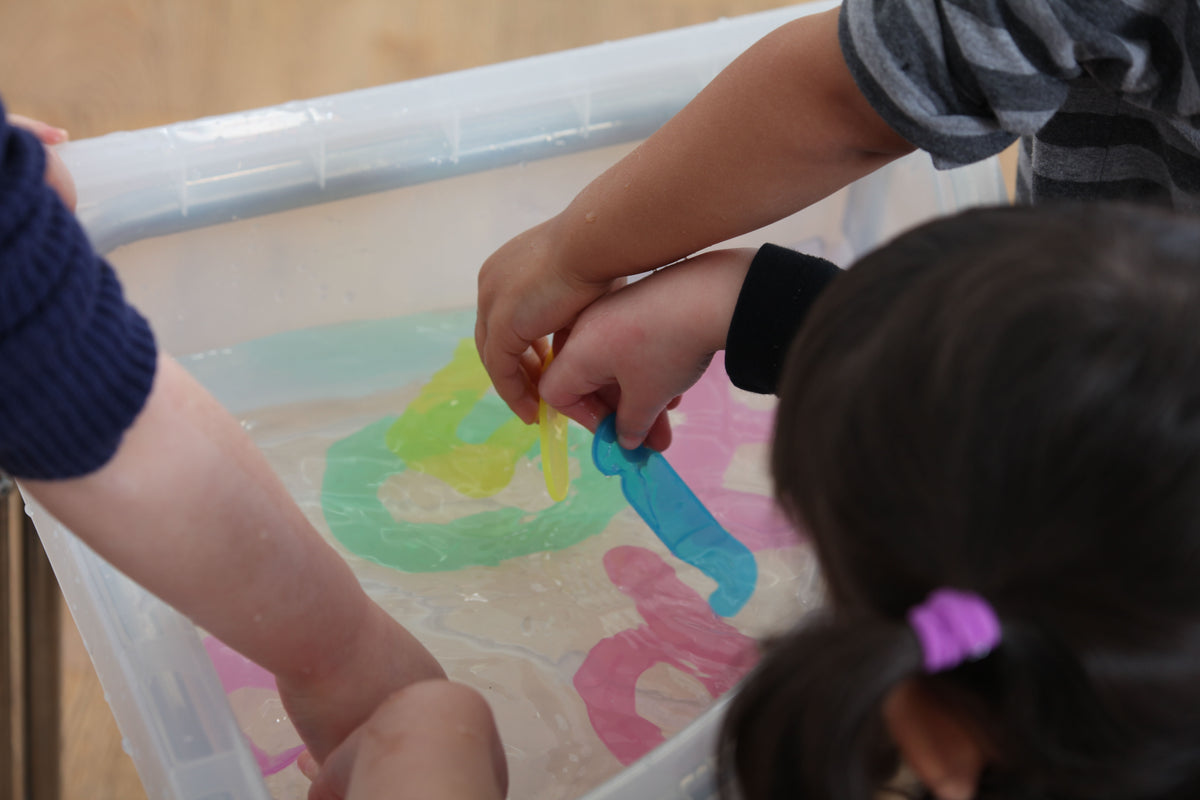 Alphabet tracing tray with colorful letter shapes under kids' hands