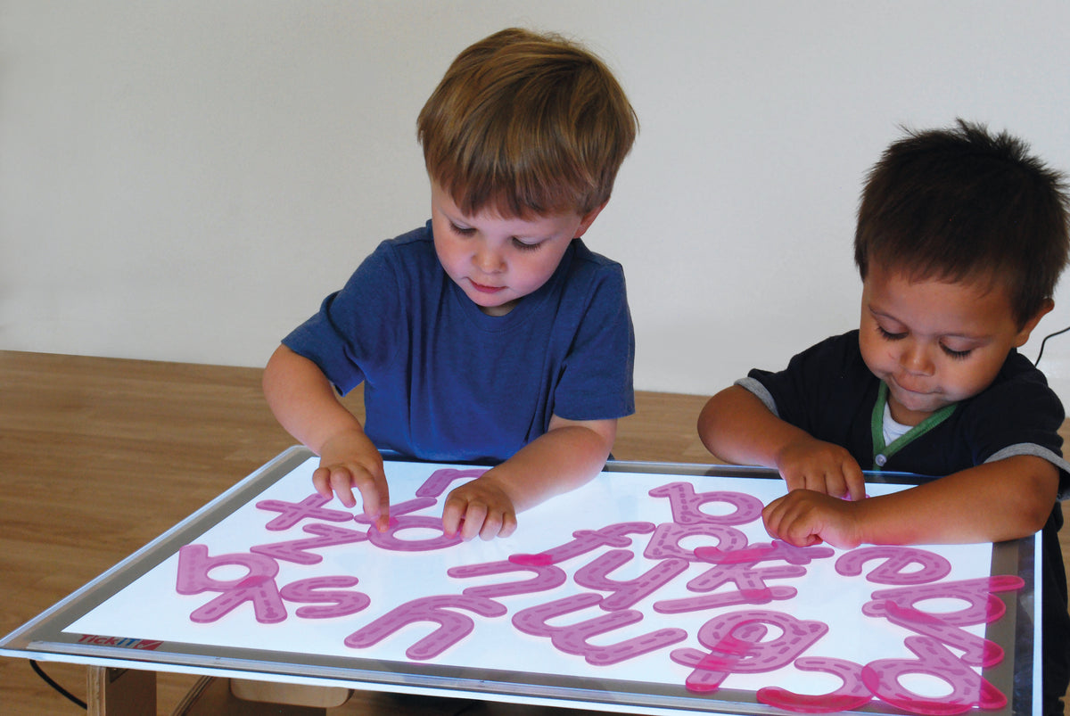 Alphabet tracing activity tray with pink letters traced by two children