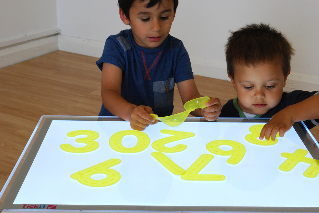 Two children tracing with yellow foam number pieces on a large writing pad