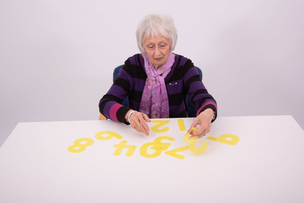 Elderly person tracing yellow foam number pieces on a table
