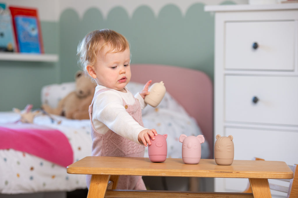 Baby playing with pastel animal-shaped silicone squirter toys on a table.