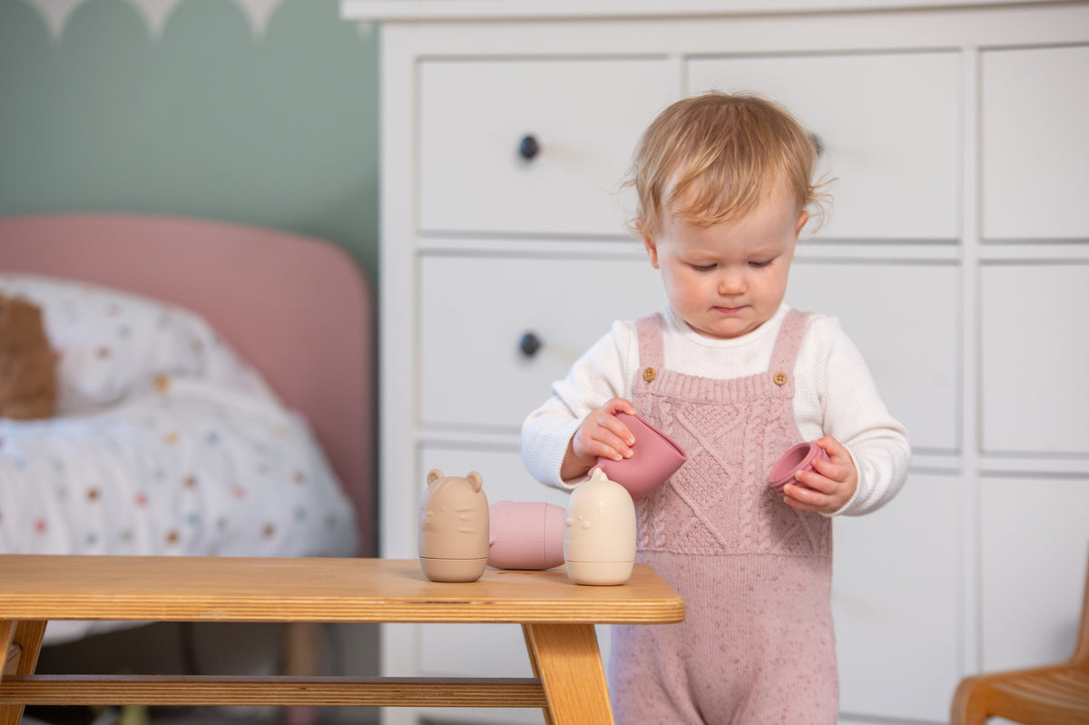 Baby standing with animal-shaped silicone squirter toys in pastel colors.