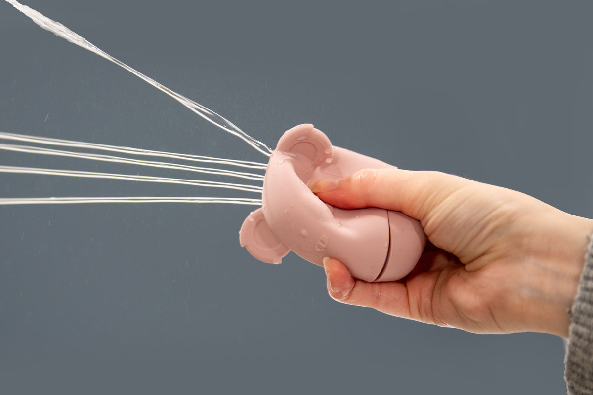 Pink bear-shaped silicone squirter toy held in hand, spraying water.