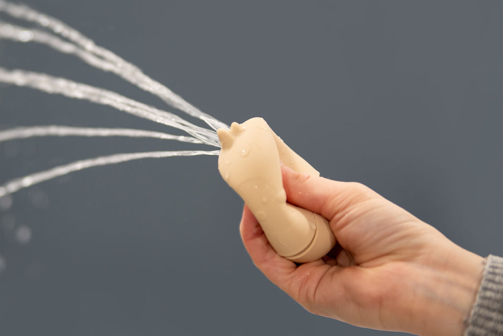 Beige animal-shaped silicone squirter toy held in hand with water stream.