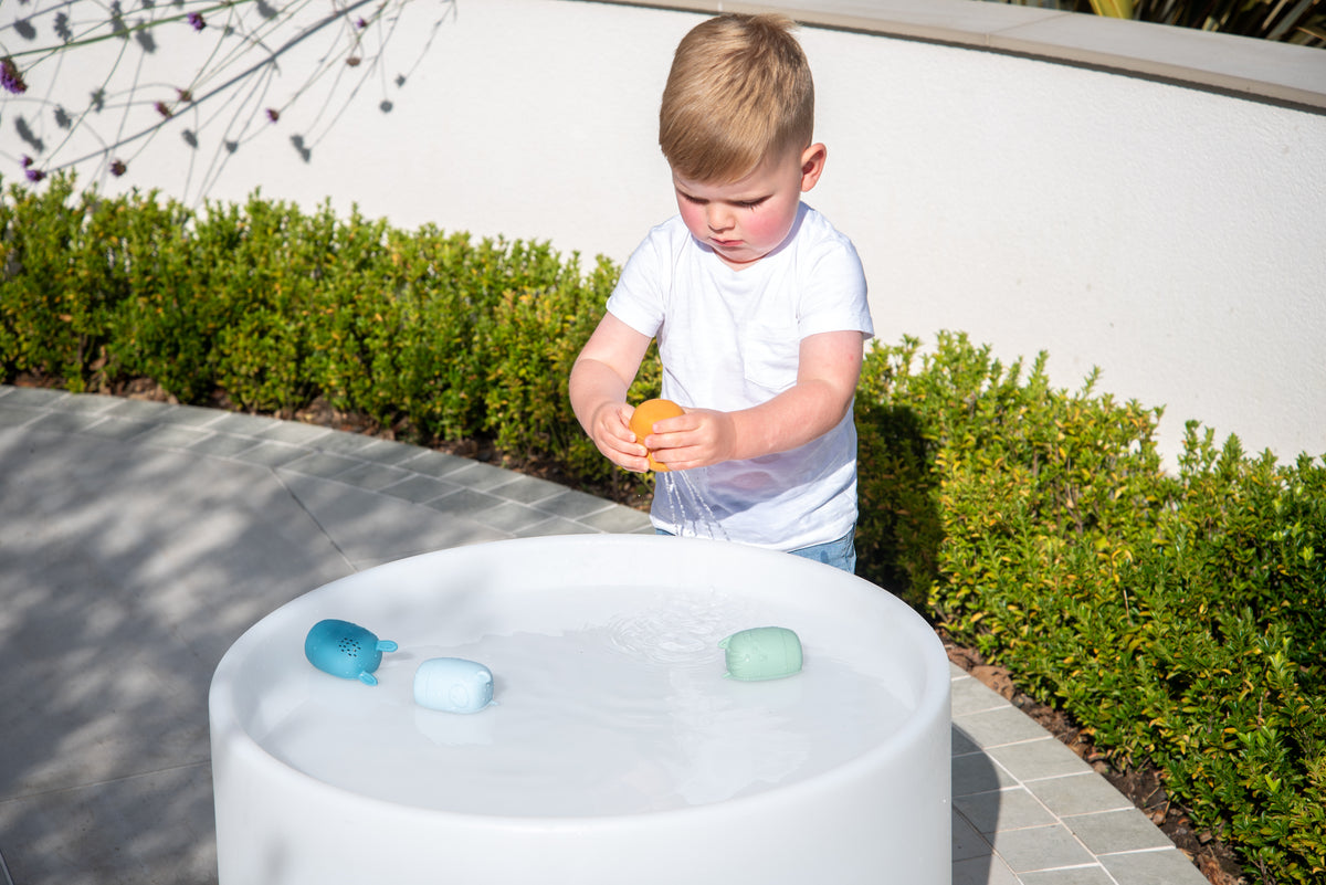 Animal squirter toys floating in an outdoor water tub: blue and green cups