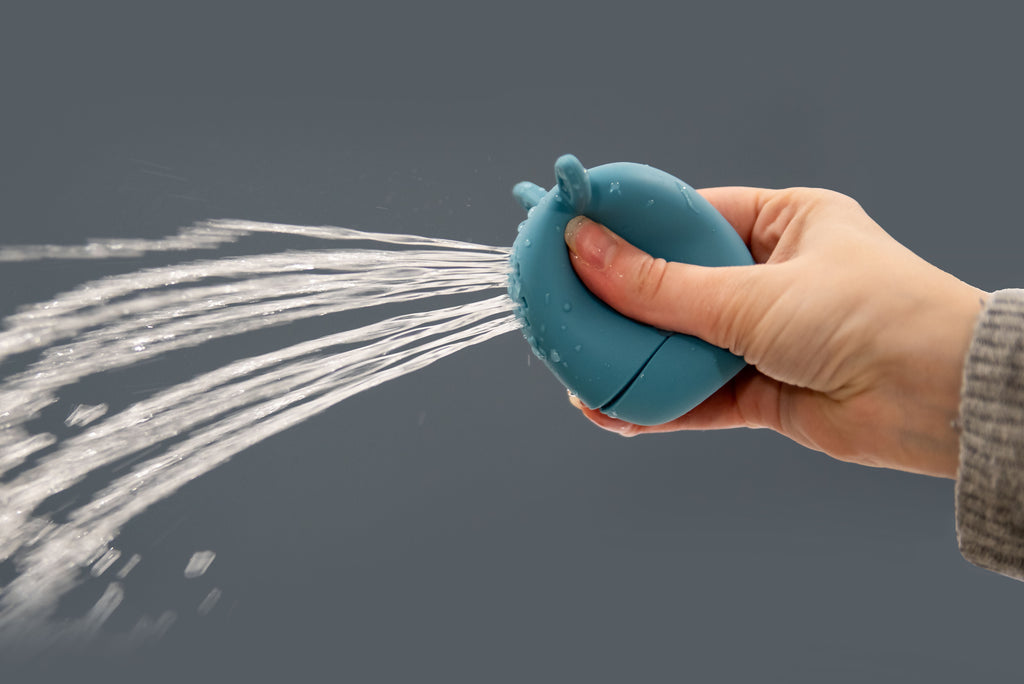 Blue animal squirter toy squeezing a water stream from the spout, held in hand