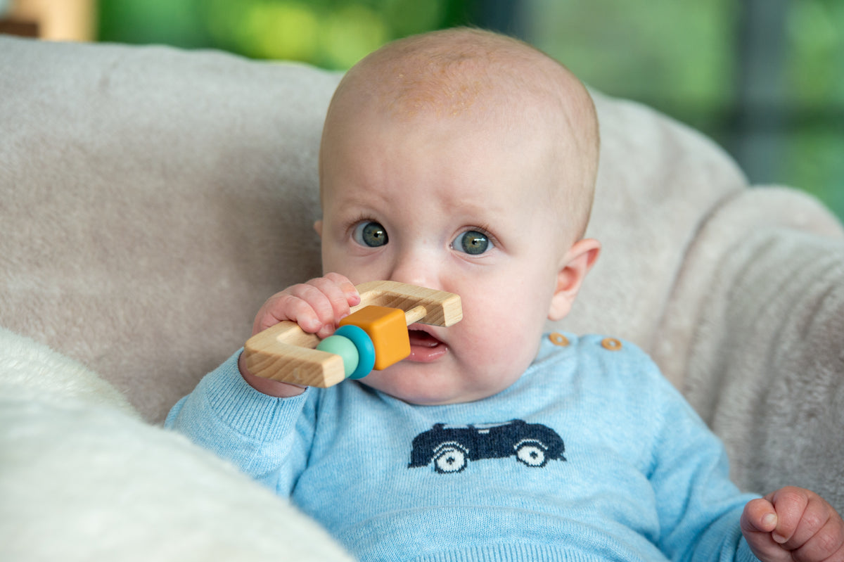 Baby holding wooden arch rattle with orange and teal beads on light wood
