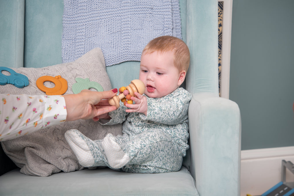 Baby reaching for wooden bead rattle with pastel beads