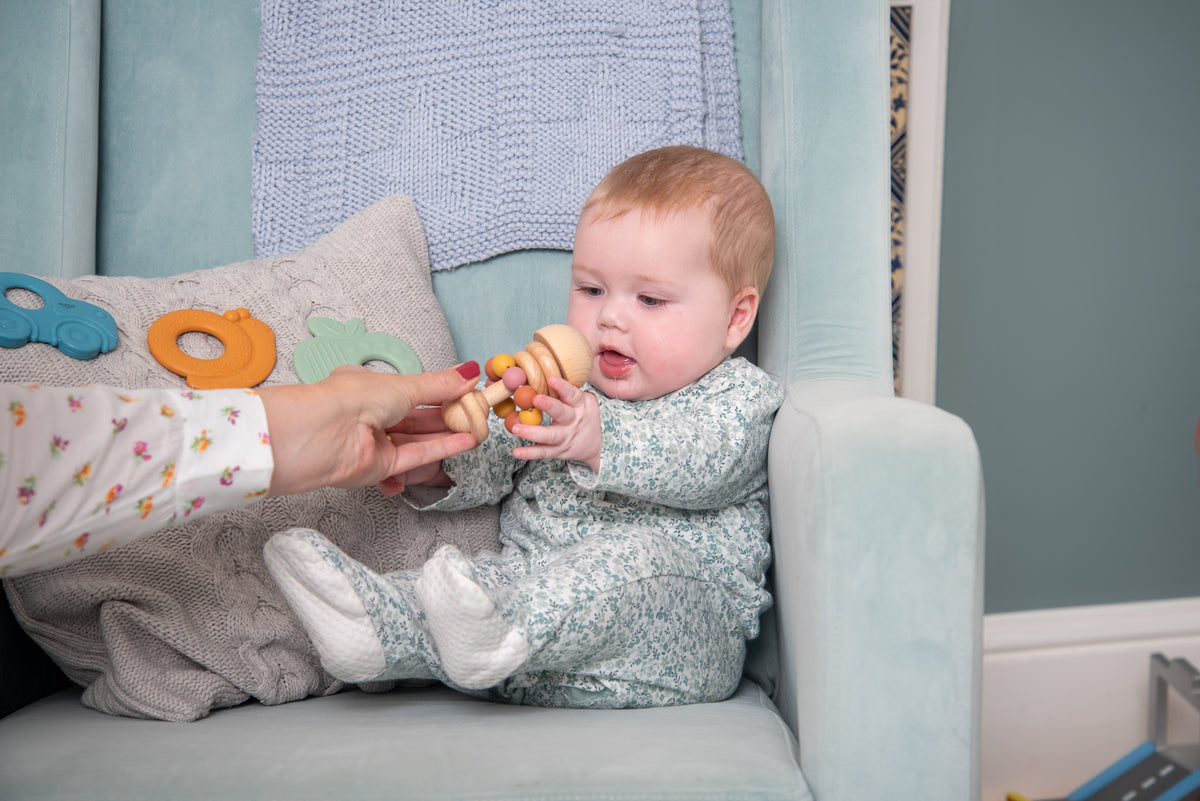 Baby reaching for wooden bead rattle with pastel beads