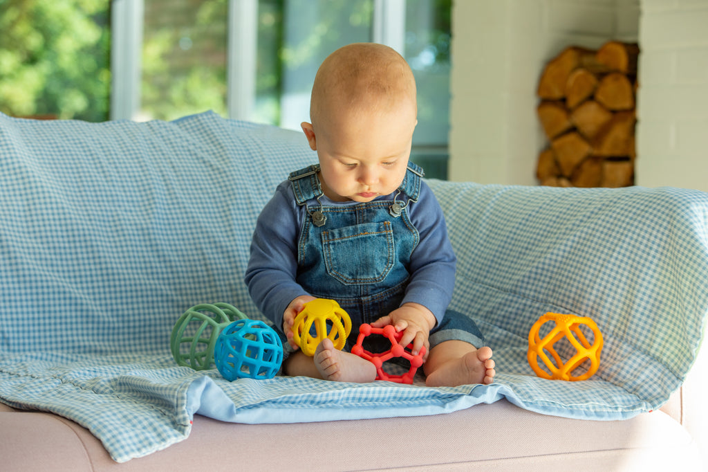 Rainbow flexi ball toy set; baby sits on a couch with colorful textured balls
