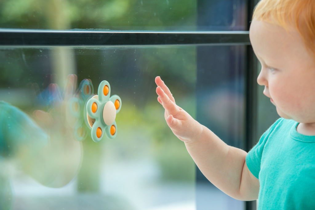 Window flower spinner toy, teal petals with orange centers, child pointing at it