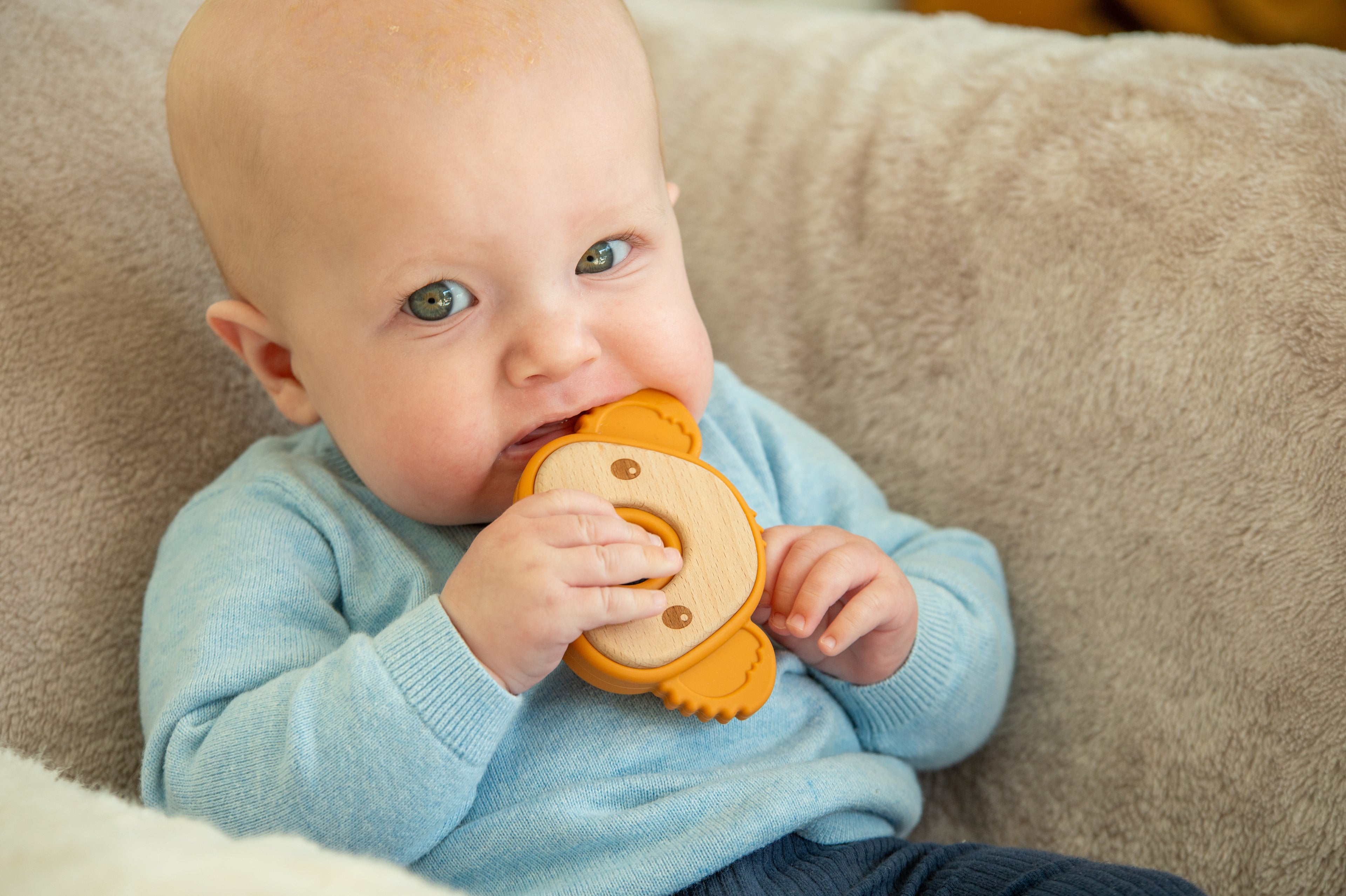 Baby holding orange koala teether with round center ring and molded side grips