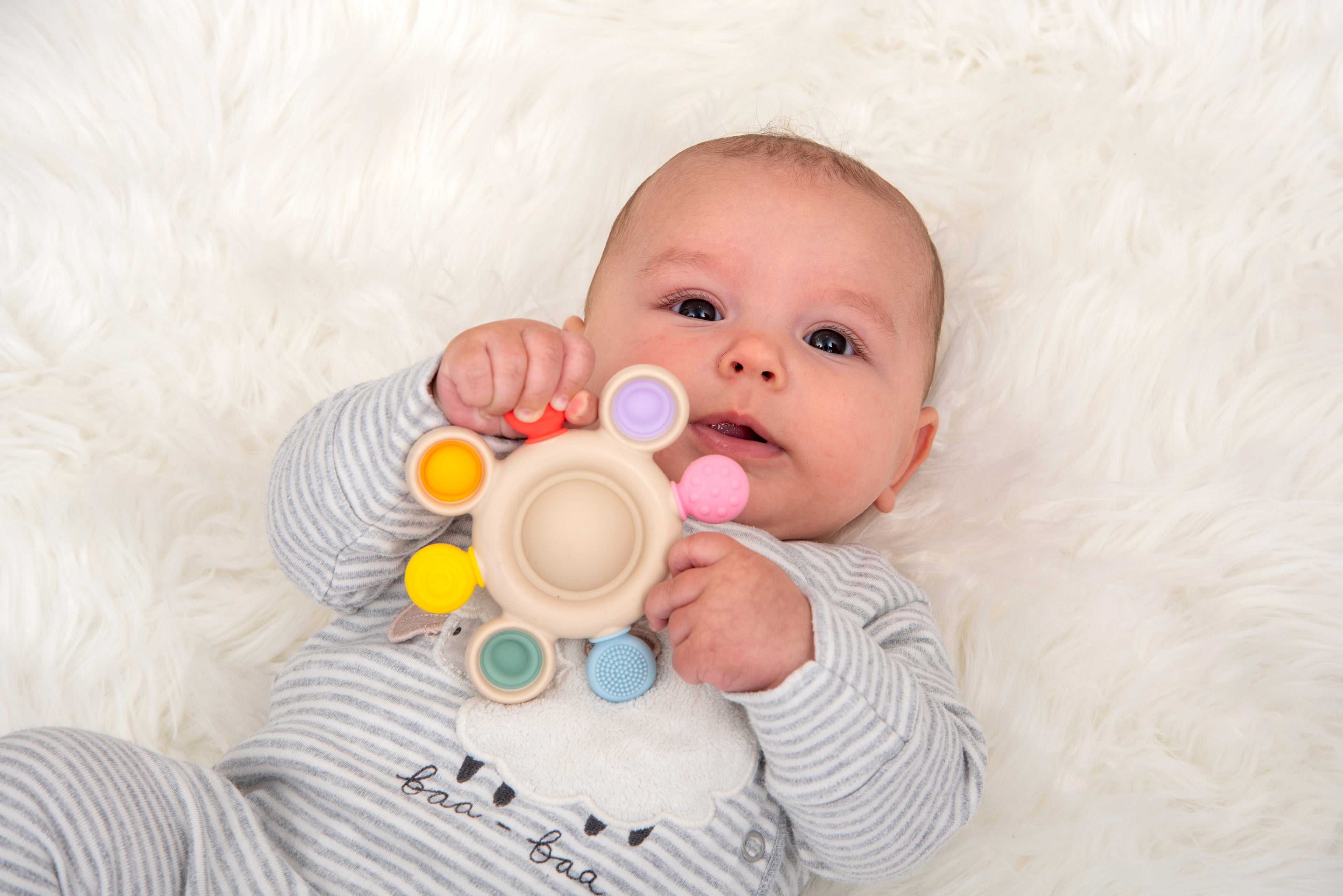Rainbow silicone pop teether with beige center, colorful rings, and textured grip