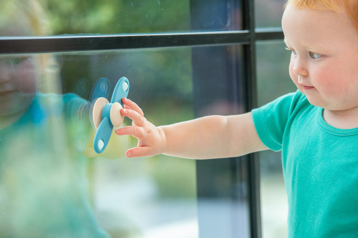 Propeller spinner toy in a child’s hand, blue handles with beige central disc