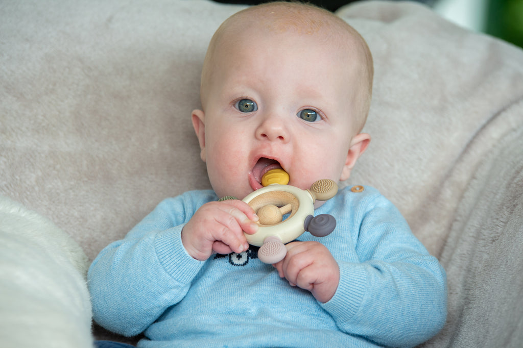 Baby holding wooden ring teether with soft fabric links on a couch