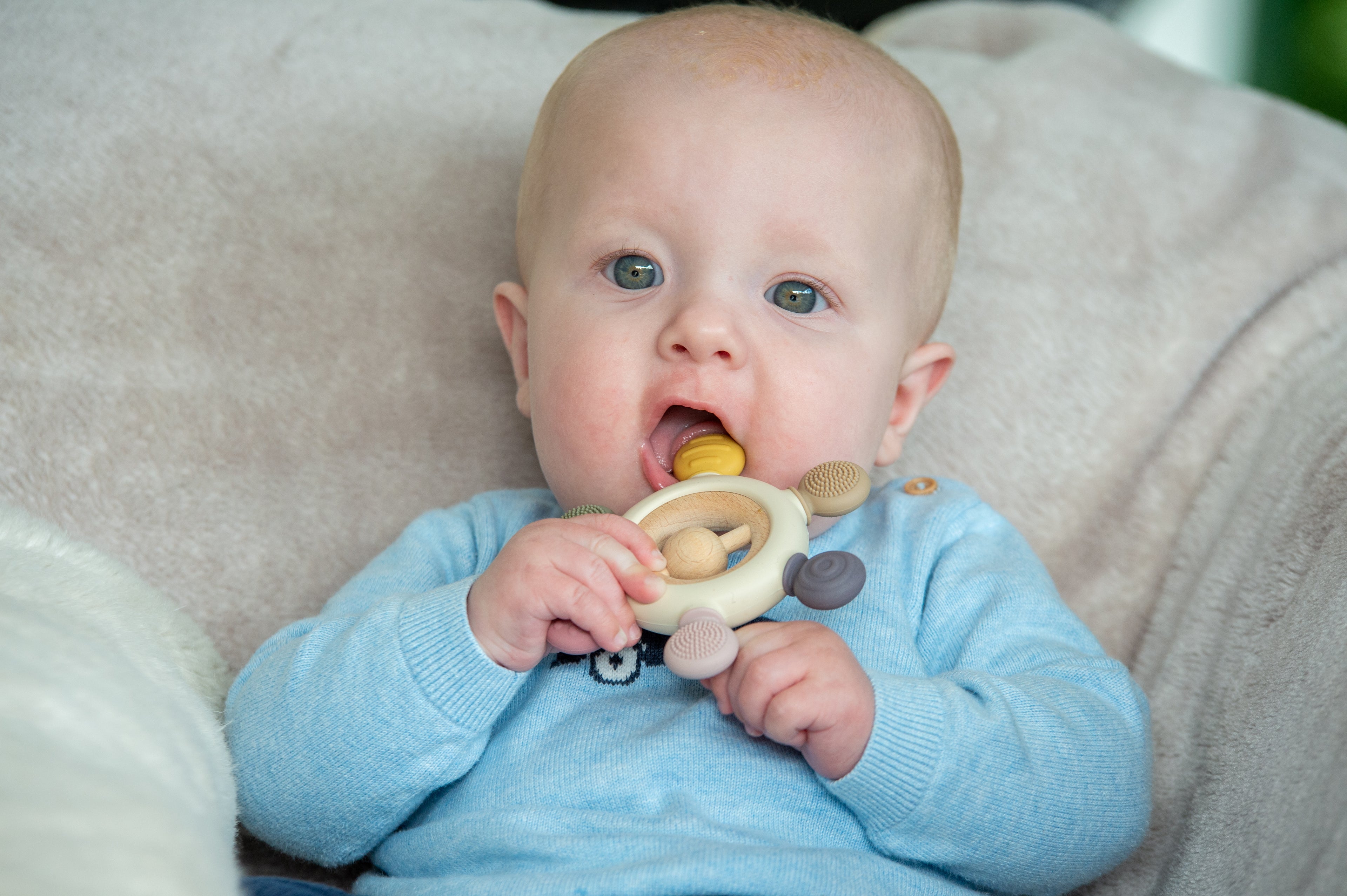 Baby holding wooden ring teether with soft fabric links on a couch