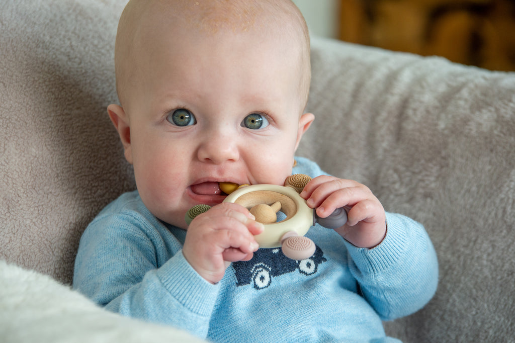 Baby holding wooden ring teether rattle near mouth with fabric bead details