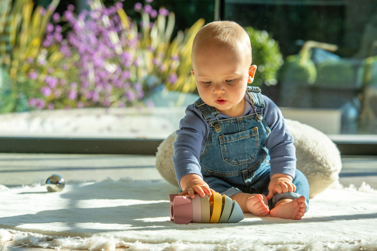 Baby playing with earth-tone rocket stacker toy on a soft blanket