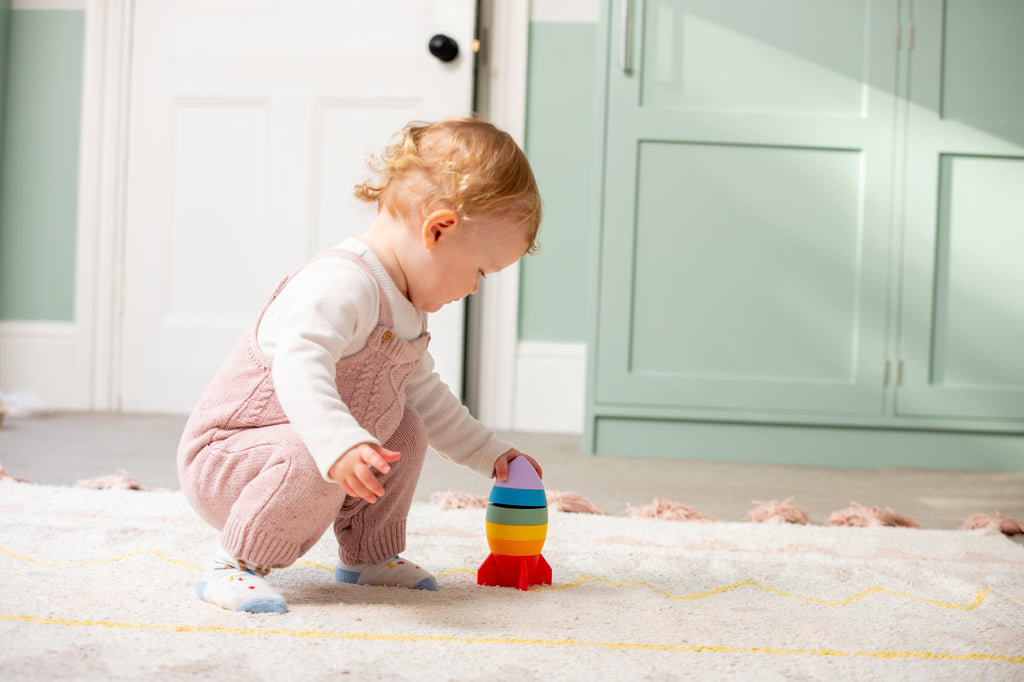 Rainbow rocket stacker toy with layered colors as a child kneels and plays.