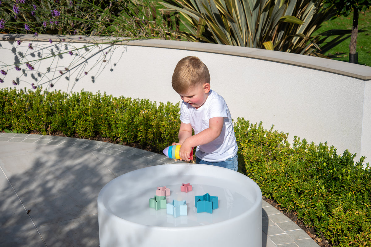 Child building with rainbow rocket stacker toy inside a white outdoor tub.