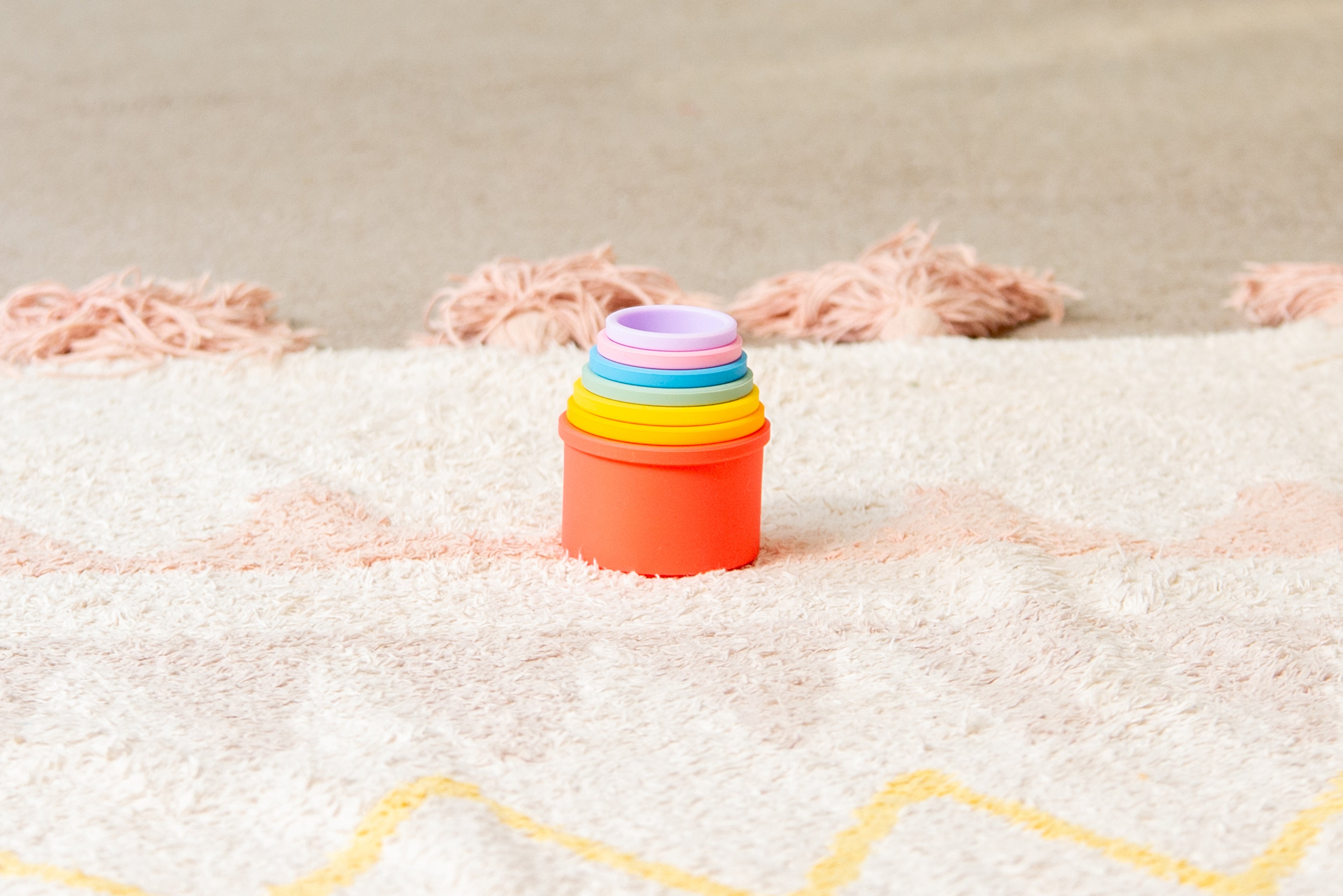Orange silicone stacking cups with nested rainbow rings on a rug