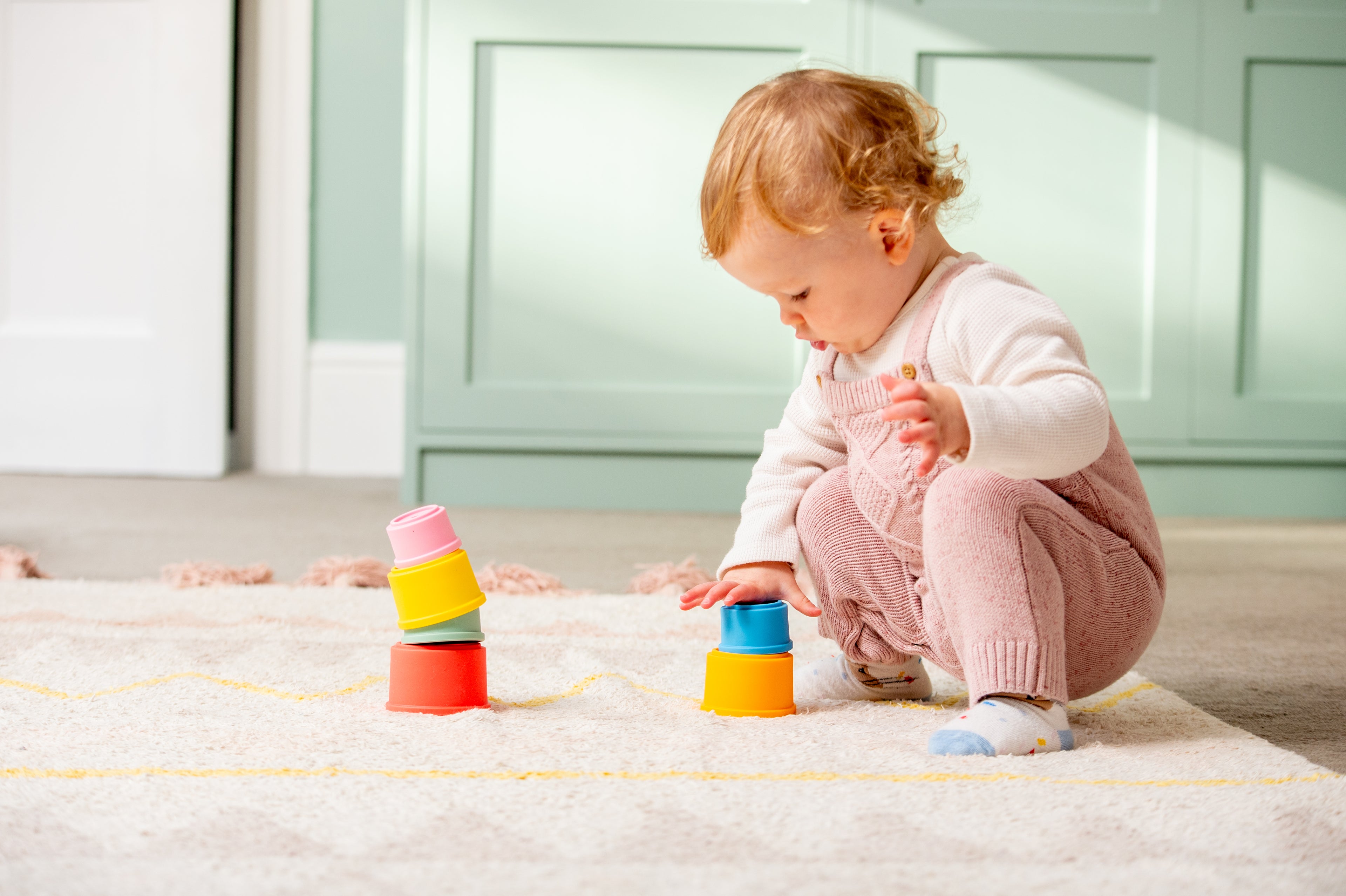 Rainbow silicone stacking cups on the floor near a toddler
