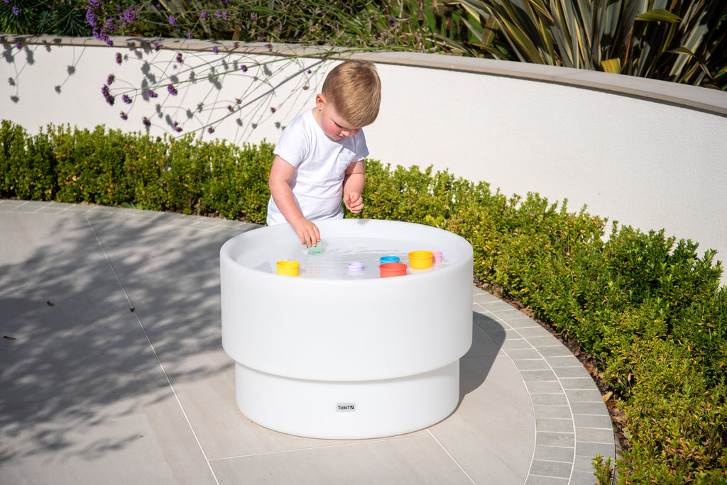 Rainbow silicone stacking cups inside a round white tub on a patio