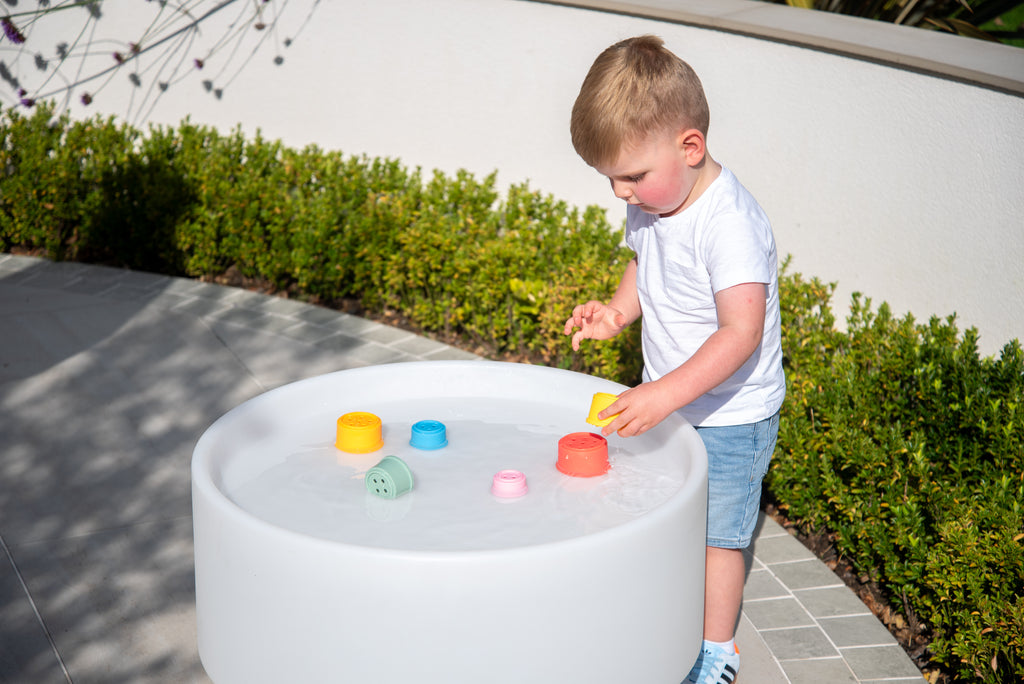 Rainbow silicone stacking cups in a round white play tub